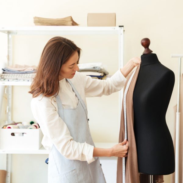 brunette-seamstress-apron-measuring-beautiful-fabric-black-dummy-workshop